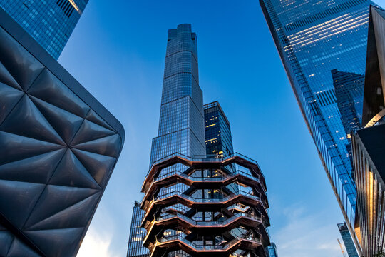 New York, NY - US - Jul 20, 2026 Impressive low-angle shot of the Vessel at Hudson Yards, surrounded by modern skyscrapers under a clear blue twilight sky, showcasing New York's architecture.