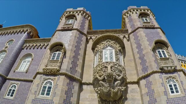 Low angle view revealing the detailed facade of the romanticist pena palace, featuring the mythological triton archway and traditional portuguese azulejo tiles against a clear blue sky