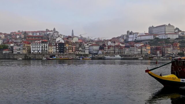 Historical ribeira district houses lining the douro river waterfront in porto, portugal, with traditional rabelo boats moored on the water and a cloudy sky providing a tranquil backdrop