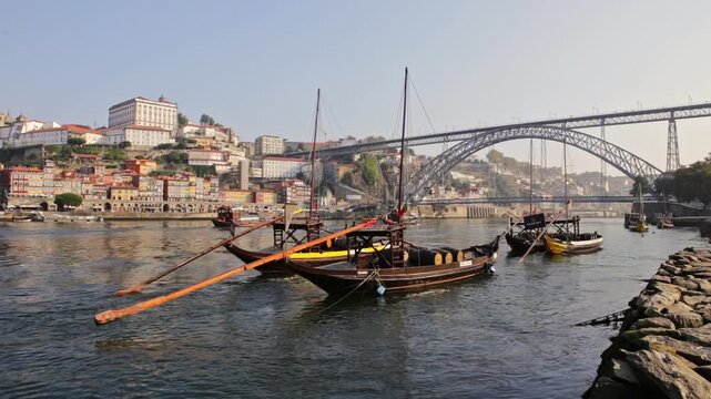 Iconic rabelo boats, traditional portuguese cargo vessels, floating on the douro river with the historic ribeira district and the dom luis i bridge in the background on a sunny day