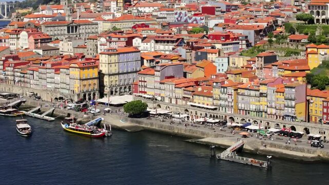 Aerial view zooming out from the beautiful ribeira district in porto, portugal, revealing the colorful buildings, the douro river with boats, and the historic cityscape on a sunny day