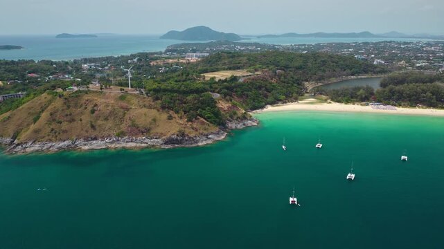 Phuket coastal landscape featuring turquoise waters of Nai Harn Beach. Travel and explore Thailand's tropical nature. Catamarans moored in a calm sea bay with a sandy shore. Aerial view drone footage