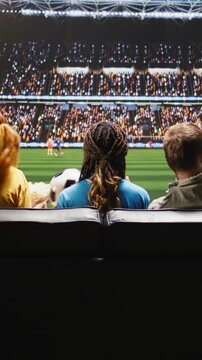 Portrait format: Football fans watch a live football match on TV from an apartment sofa, feeling transported to a stadium field by lifelike experiential broadcasting.