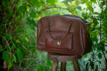 Vintage leather bag in lush garden setting - perfect accessory for travel adventures and natural photography themes © Hanna
