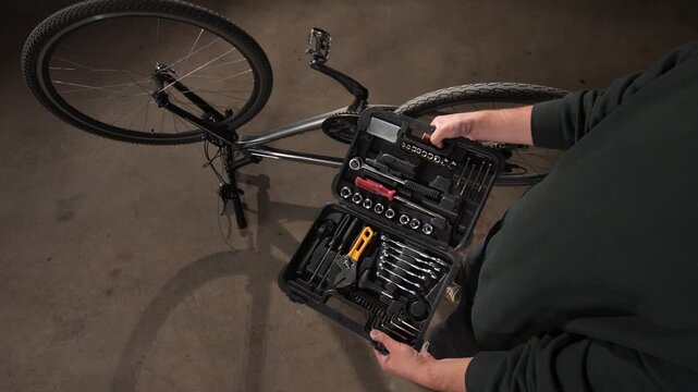 High angle view person is opening a comprehensive tool kit filled with various hand tools. Including wrenches and screwdrivers. Preparing to fix a bicycle lying upside down on the workshop floor