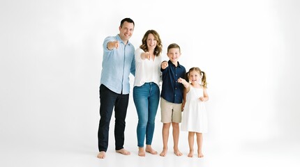 Fototapeta premium Happy family of four standing together in white studio, smiling parents and two adorable children pointing forward with index fingers, casual lifestyle portrait photography, family unity concept