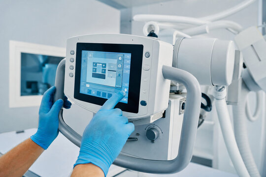 Finger in blue glove tapping touchscreen control console of x-ray machine. Setting exposure parameters on digital radiography equipment in hospital. Generative AI.