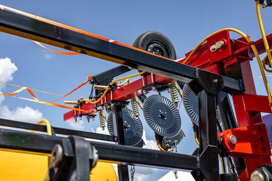 Agricultural machinery disc openers furrow openers mechanism. Modern farm equipment seeder coulter parts assembly on red metal chassis and industrial transport vehicle engineering technical details.