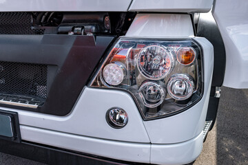 Semi truck front LED headlight block with fog light lens. Commercial vehicle white plastic bumper shell detail view with radiator grill panel and long haul transport tractor engineering details. © NastyaPhoto