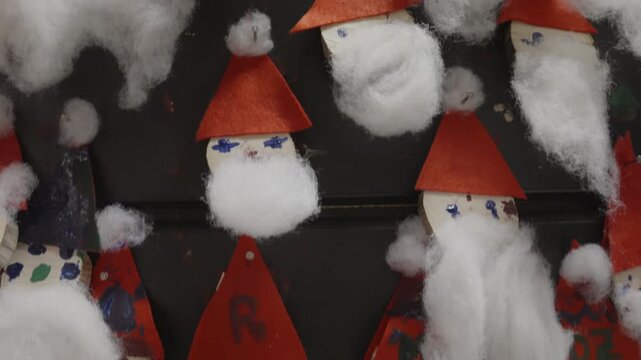Handmade Santa Claus ornaments made from wood slices with white cotton beards and small red felt hats, arranged on a dark board