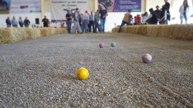 Medium shot of a bocce ball court focused on the jack as unrecognizable players compete around it. Outdoor precision sport, recreation, strategy, friendly competition and leisure