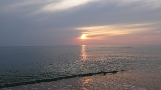 Atmospheric Sunrise View Over Shoreline Waves.
Dramatic and peaceful early morning sky with the sun glowing behind light clouds above gentle waves lapping on the beach sand.