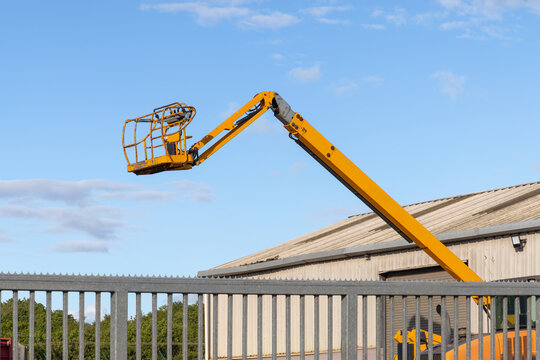 Yellow cherry picker boom lift raised above an industrial unit against blue sky