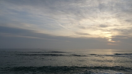 Fototapeta premium Wide Morning Sky with Soft Cloud Layers and Quiet Sea Wave. Panoramic view capturing vast textured clouds illuminated by a subtle sunrise glow above gentle waves on the Gangneung coast.