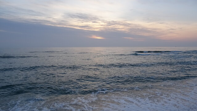 Soft Morning Glow Behind Clouds Over Quiet Sea at Dawn.
Gentle dawn light peeking through subtle cloud layers over a tranquil ocean with soft foaming waves breaking along the beach.