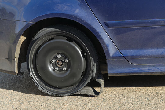 Shredded tyre disintegrated from the rim of a blue car on a road