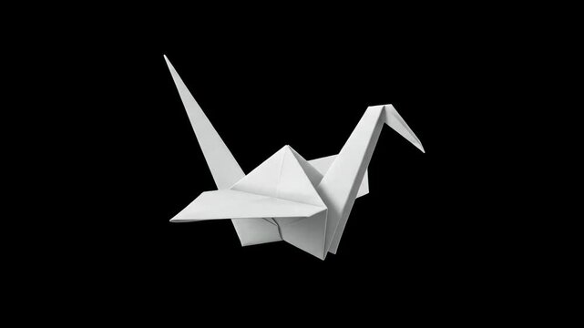 A classic white paper origami crane bird isolated against a solid black background. Ideal for Japanese cultural videos, paper craft tutorials, peace symbol graphics, minimalist design projects, and el