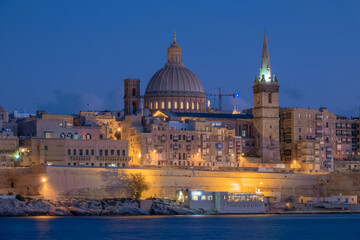 Naklejka premium Valletta Malta at Blue Hour: Illuminated Cathedral Dome and Fortress Wall Long Exposure | Historic Baroque City Skyline Waterfront at Night | Mediterranean Old Town Nightscape