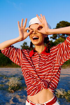 Happy woman lifestyle portrait in striped shirt posing on beach. Creative person making goggles with hands, laughing, having fun. Concept of summer vacation, travel, freedom and joy.