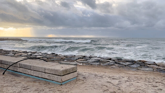 Rough sea advancing toward the concrete seawall and sandy beach of Furadouro under a dramatic stormy sky in Ovar Portugal