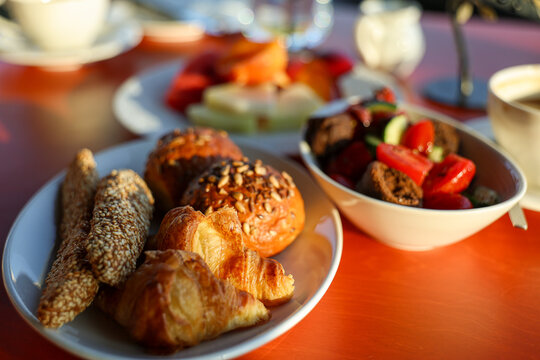 Assorted pastries, breadsticks, salad, and fruit served for breakfast at a sunlit caf&eacute; in Athens, Greece.