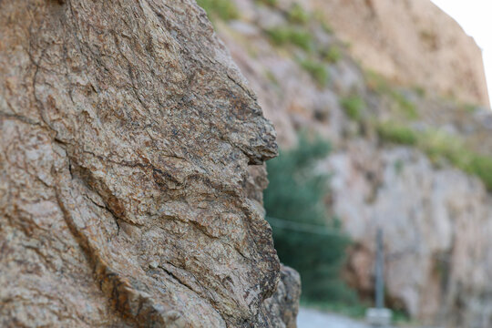 Close-up of a textured rock formation resembling a human profile with blurred rocky background and greenery seen at the Acropolis in Athens, Greece.