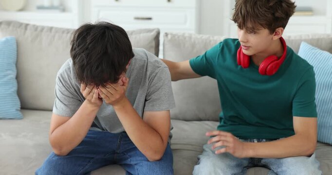 Teenage boy supporting his sad brother on sofa at home. Camera moving forward