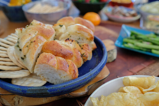 Garlic bread, appetizer, party food, sliced bread, focaccia, crackers, snack served on a blue ceramic plate during a gourmet dinner party or a social gathering at a rustic home.