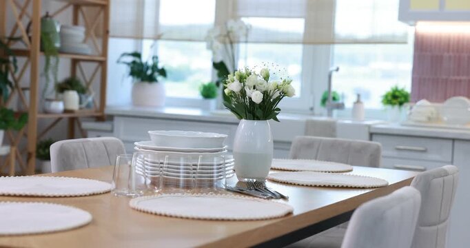 Stylish setting with vase of flowers, plates and glasses on wooden table in kitchen. Camera moving