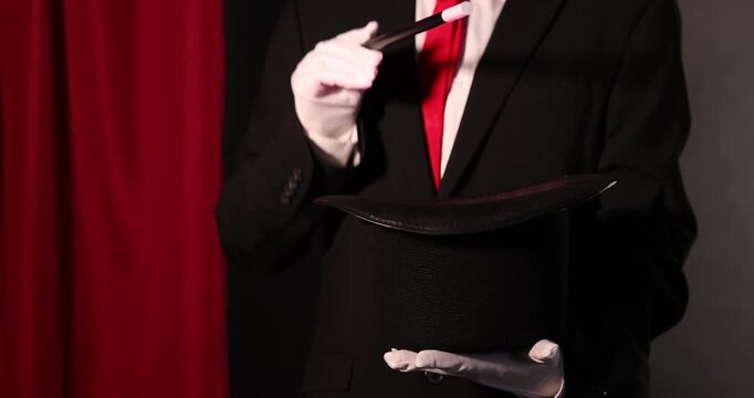 Magician showing trick with wand and top hat on stage, closeup