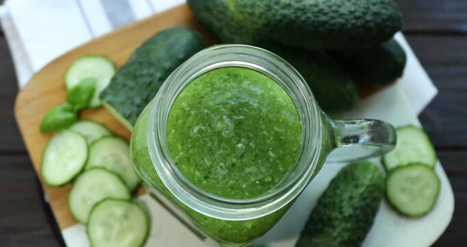 Delicious smoothie in mason jar, fresh cucumbers and basil on table, rotating