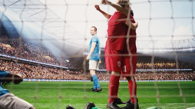 Red team players scoring goal and defeating opponents in soccer match, goalkeeper disappointed by missed save, goal scorer shooting winning goal, teammate celebration.