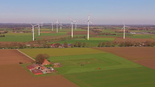 Beautiful high altitude aerial panoramic perspective of countryside agricultural farmland traditional red roof farmhouses and wind turbines under a clear blue sky in bright daylight