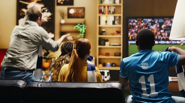 Angry football supporters watching match on TV scolding players after missed goal scoring chance with frustrated soccer fans showing negative emotion.