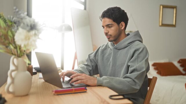 Man typing on laptop with hands on keyboard and smiling, points finger in a later frame at camera in a bright bedroom desk area; productivity remote work.