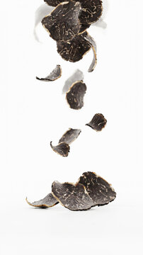 Black truffle slices levitating above a pile on a white background