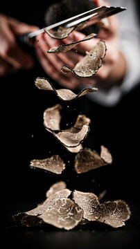 Black truffle levitating above a chef's hand with slicing tool in dark setting