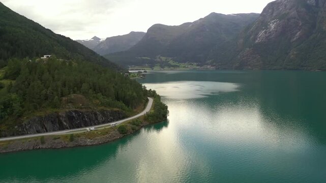 Scenic road along fjord lake in Stryn, Norway, with steep mountains and reflective still water under soft daylight