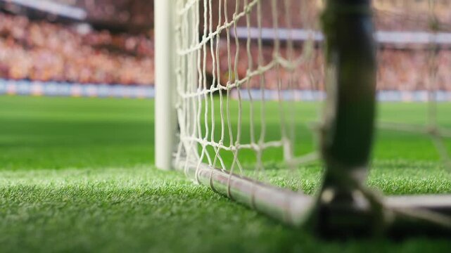 Close focus on soccer goal net showing rope knots and grid texture against blurred stadium field, selective focus during football match, soccer pitch perspective, for football match content.