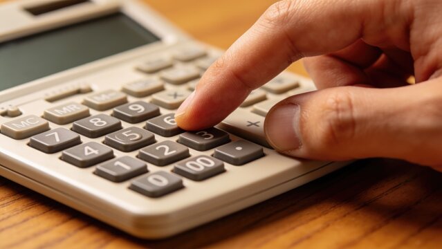 Close-up of hand using calculator for calculations on wooden desk