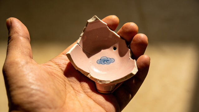 Hand holding broken pink ceramic shard with blue cloud design, ancient artifact