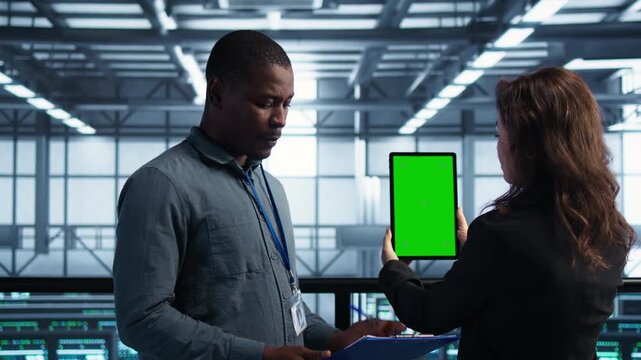 Technicians use tablet for green screen in a data center, linking screen mockup, technical documentation and infrastructure work within a controlled technical environment.