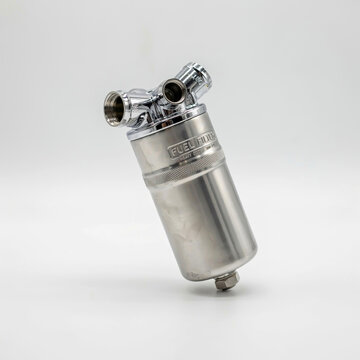 Chrome and stainless steel fuel filter with threaded connectors on white automotive engine