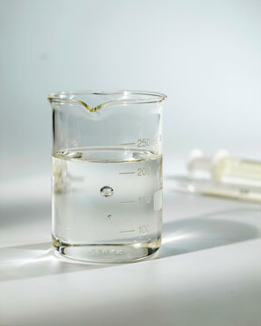 Glass beaker with clear liquid and bubbles on a white surface with blurred syringe laboratory