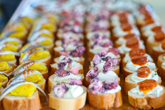 Close-up of assorted bite-sized canap&eacute;s with seafood and savory toppings on toasted bread.