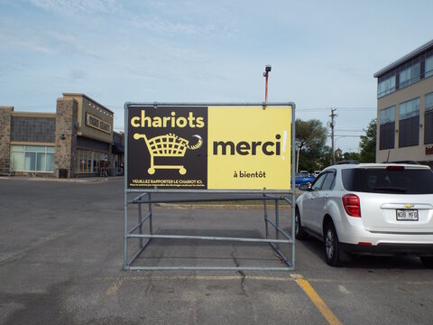 Gatineau,Quebec, Canada &ndash; June 2, 2026: A "bilingual outdoor shopping cart" return sign with English and French messaging stands in a commercial parking lot on Chem. d'Aylmer