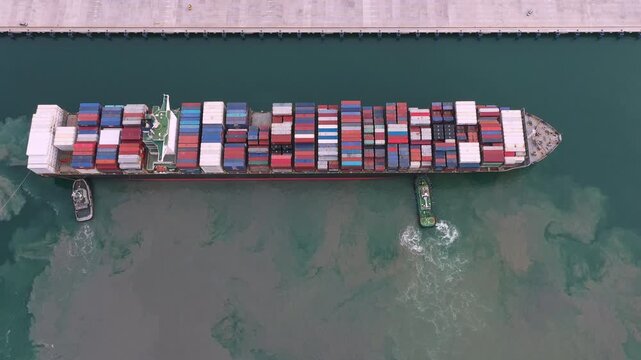 Large container ship traverses dark canal waterway at night, escorted by tow boats and marked by imposing concrete walls, generating powerful sense of scale and quiet reflection.