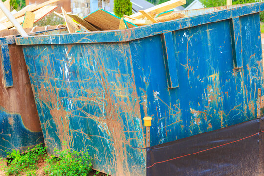 Workers place wood debris into large blue dumpster near construction site in residential neighborhood.