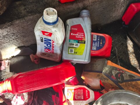 Collection of used motorcycle engine oil and gear oil bottles lying in a messy repair shop environment. Authentic photo stock for automotive service, maintenance, and workshop concepts. Brebes, August