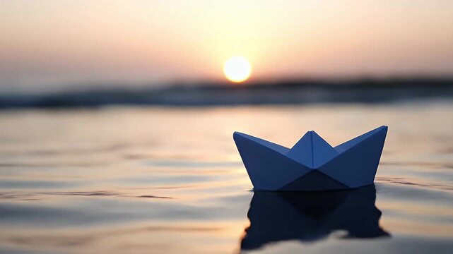 Origami paper boat floating on calm ocean water at sunset.